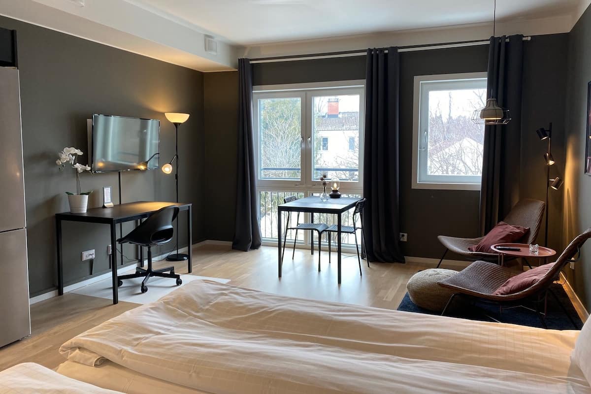 Una habitación de hotel moderna con cama, escritorio, silla y ventanas amplias.