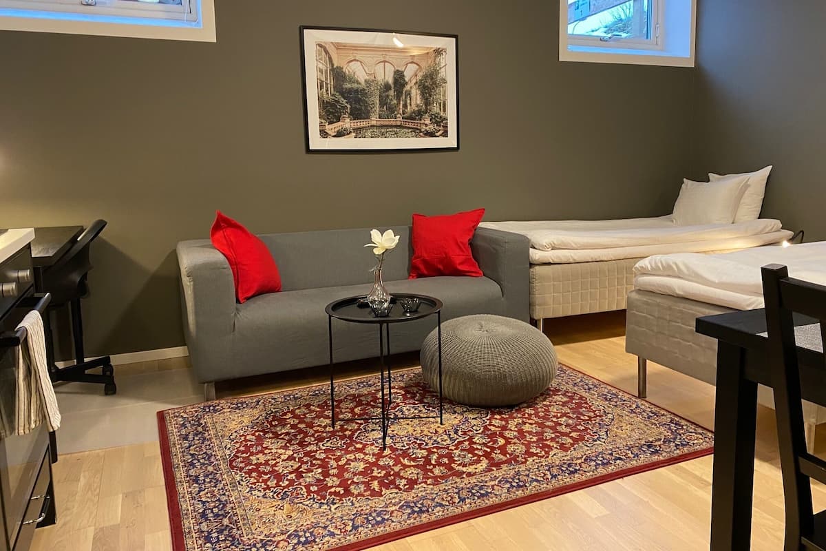Una sala de estar moderna con un sofá gris, cojines rojos, un reposapiés redondo pequeño, una mesa de centro y un cuadro enmarcado en la pared.