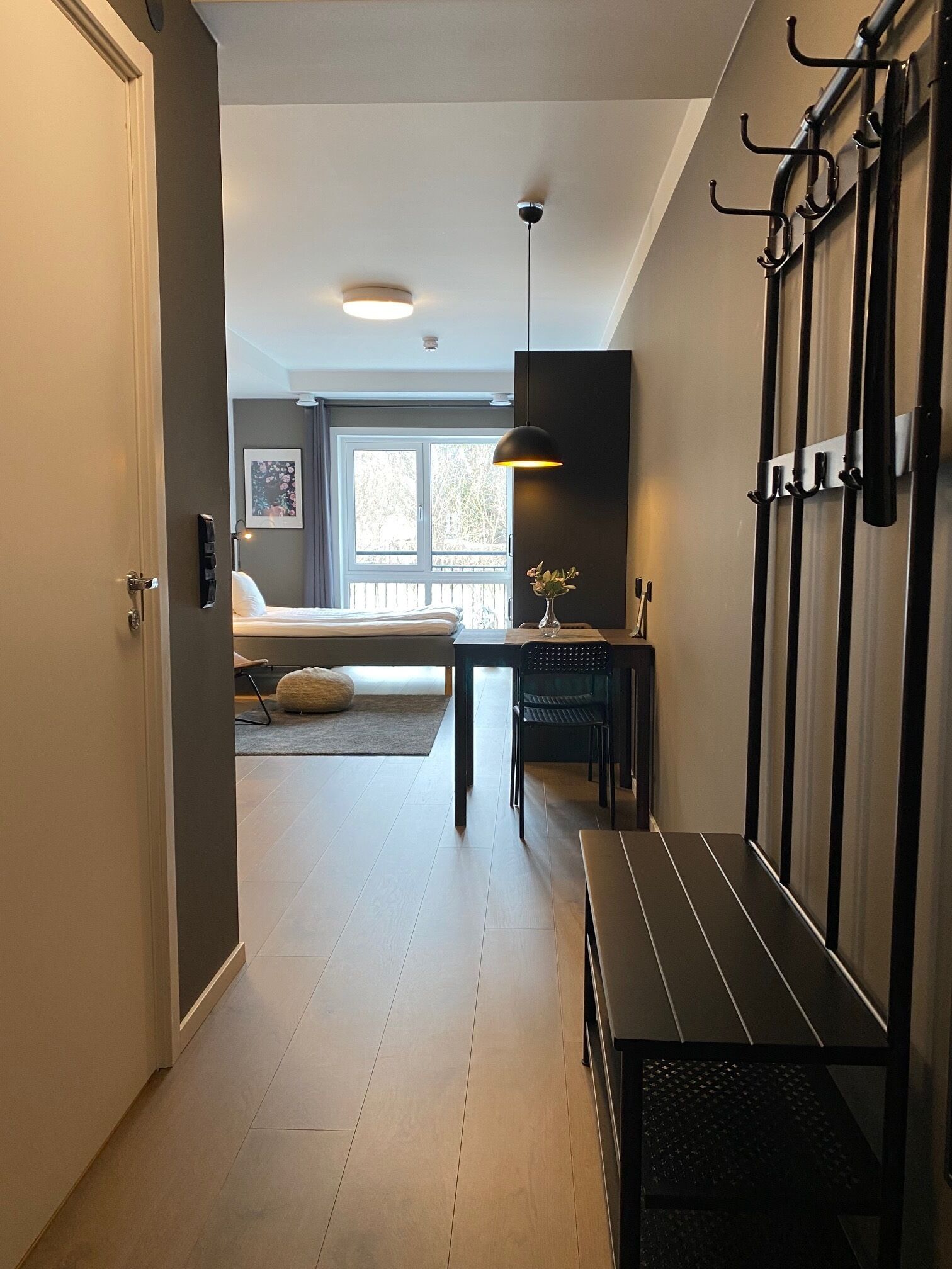 Une chambre d’hôtel moderne équipée d’un lit, d’un bureau, d’une banquette et d’un porte-manteau fixé au mur.
