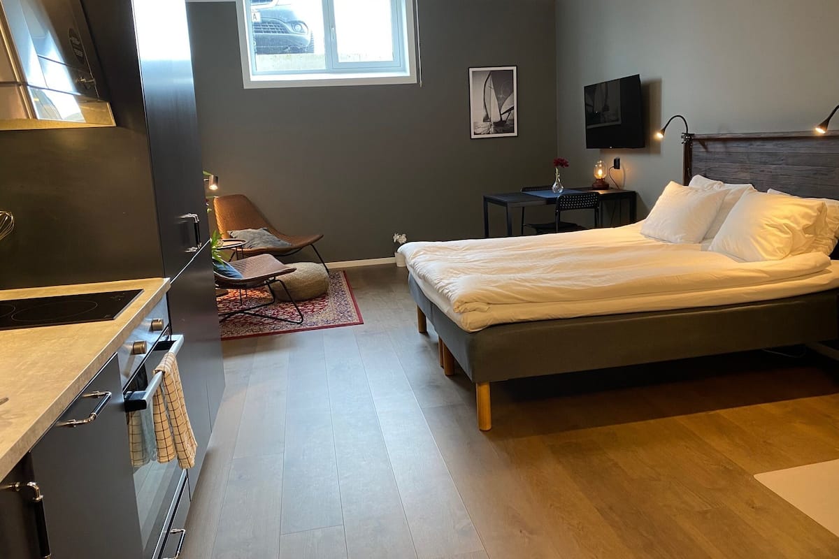 Un dormitorio moderno con cama, una silla, un escritorio y una ventana.