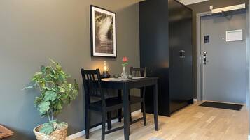 Comedor con una mesa, sillas, planta en maceta, un cuadro enmarcado y una puerta con cámara de seguridad.