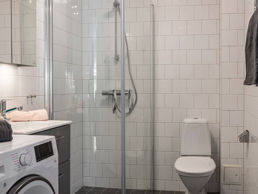 Ein modernes Badezimmer mit einer Glaskabine zur Dusche, einer Toilette und einer Waschmaschine.