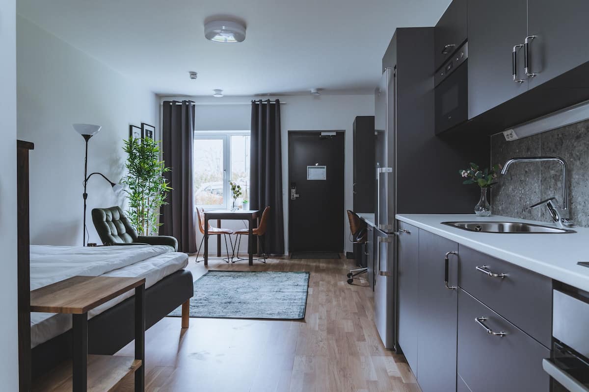 Una cocina moderna con armarios oscuros, un lavamanos de acero inoxidable y un comedor con mesa y sillas.