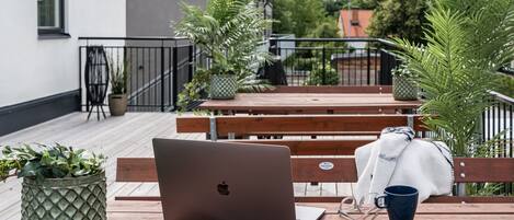 A laptop on a wooden bench with a blue mug beside it, surrounded by potted plants.