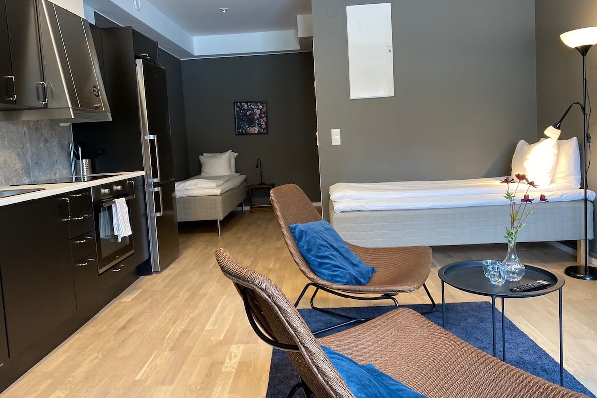 Un espacio habitable compacto con kitchenette, cama, sillón y una mesita.