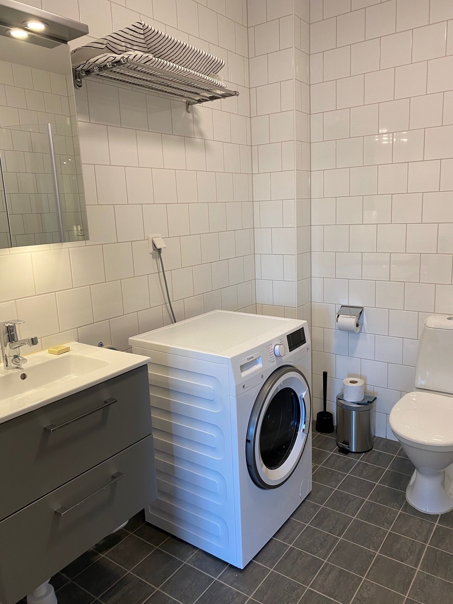 A modern bathroom with a built-in washing machine, a toilet, and a sink.