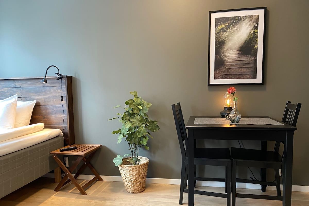 Una habitación acogedora con una cama de cabecera de madera, una mesa de comedor con sillas, una mesita auxiliar y una planta en maceta.