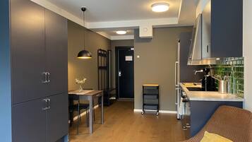 A modern kitchen with dark cabinets, a dining area with a table and chairs, a kitchen island, and a seating area with a chair and a cushion.