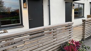 A modern building with black doors and windows, a wooden fence, and a planter with flowers. - Magnolia House Norrviken (Sollentuna)