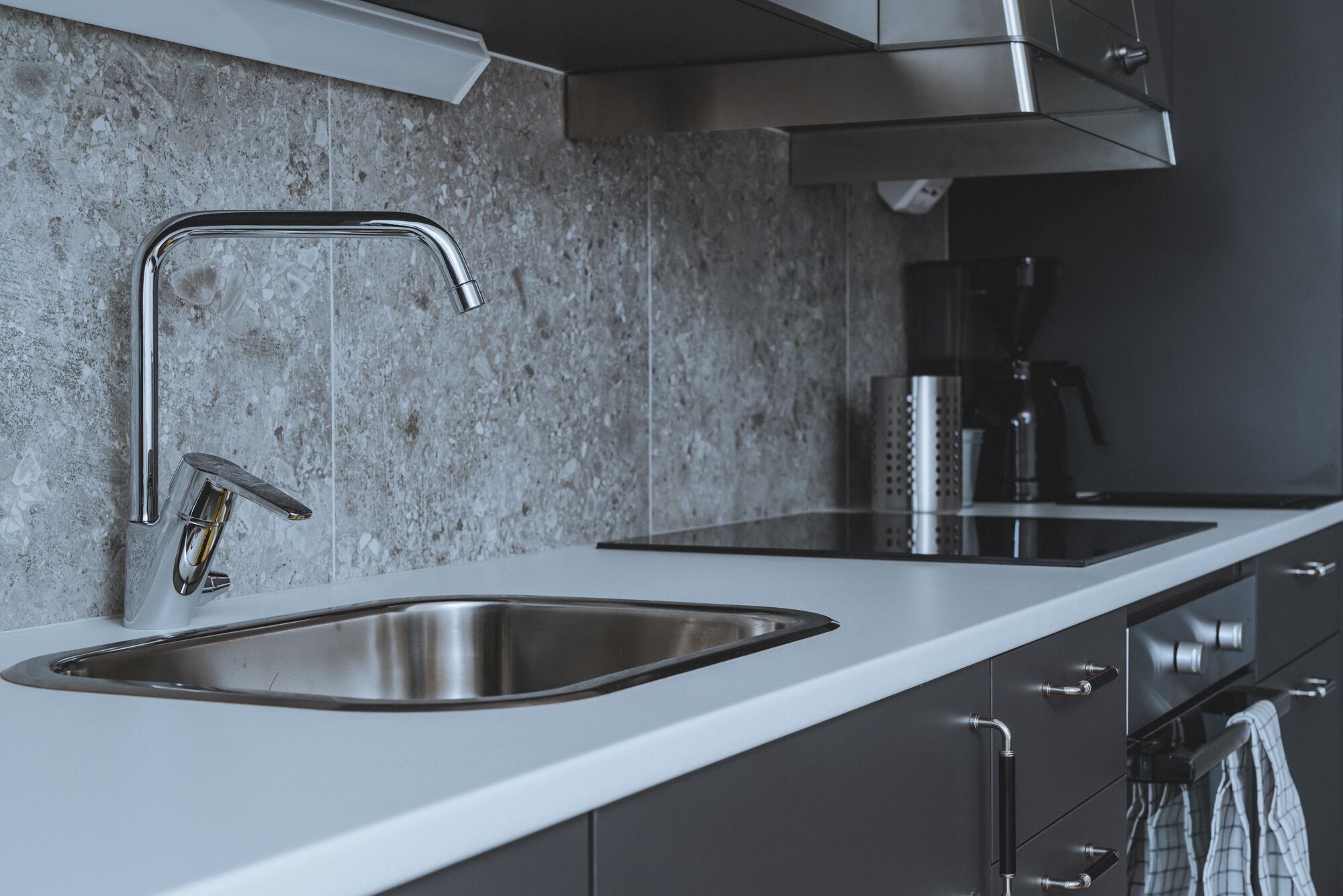 A modern kitchen with a stainless steel sink, a coffee maker, and a range hood.