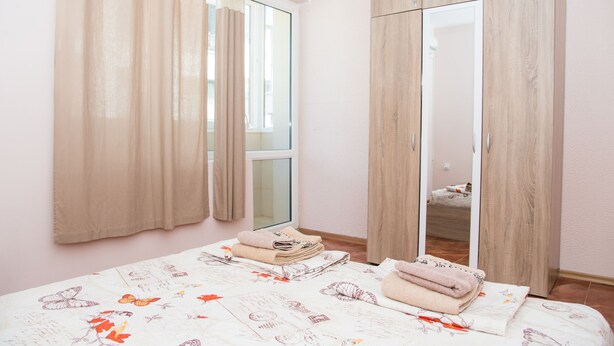 Ein Schlafzimmer mit Bett, Kleiderschrank, Spiegel und einem Fenster mit Vorhängen.