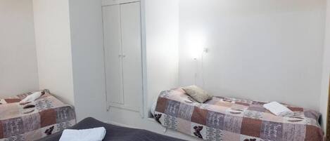 Una habitación pequeña y limpia, con dos camas, un armario y una lámpara.