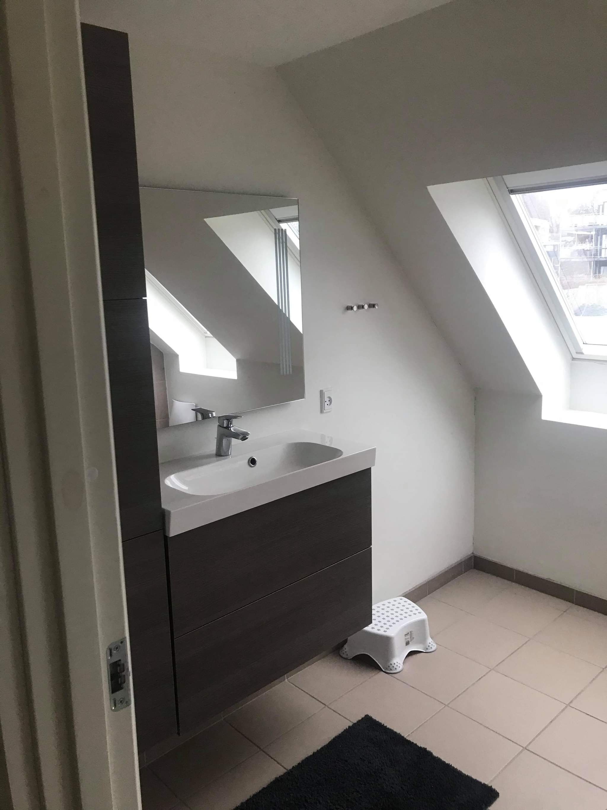 A modern bathroom with a large mirror, a sink, and a small stool.