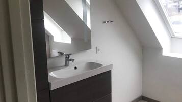 Een moderne badkamer met een grote spiegel, een wastafel en een klein krukje.