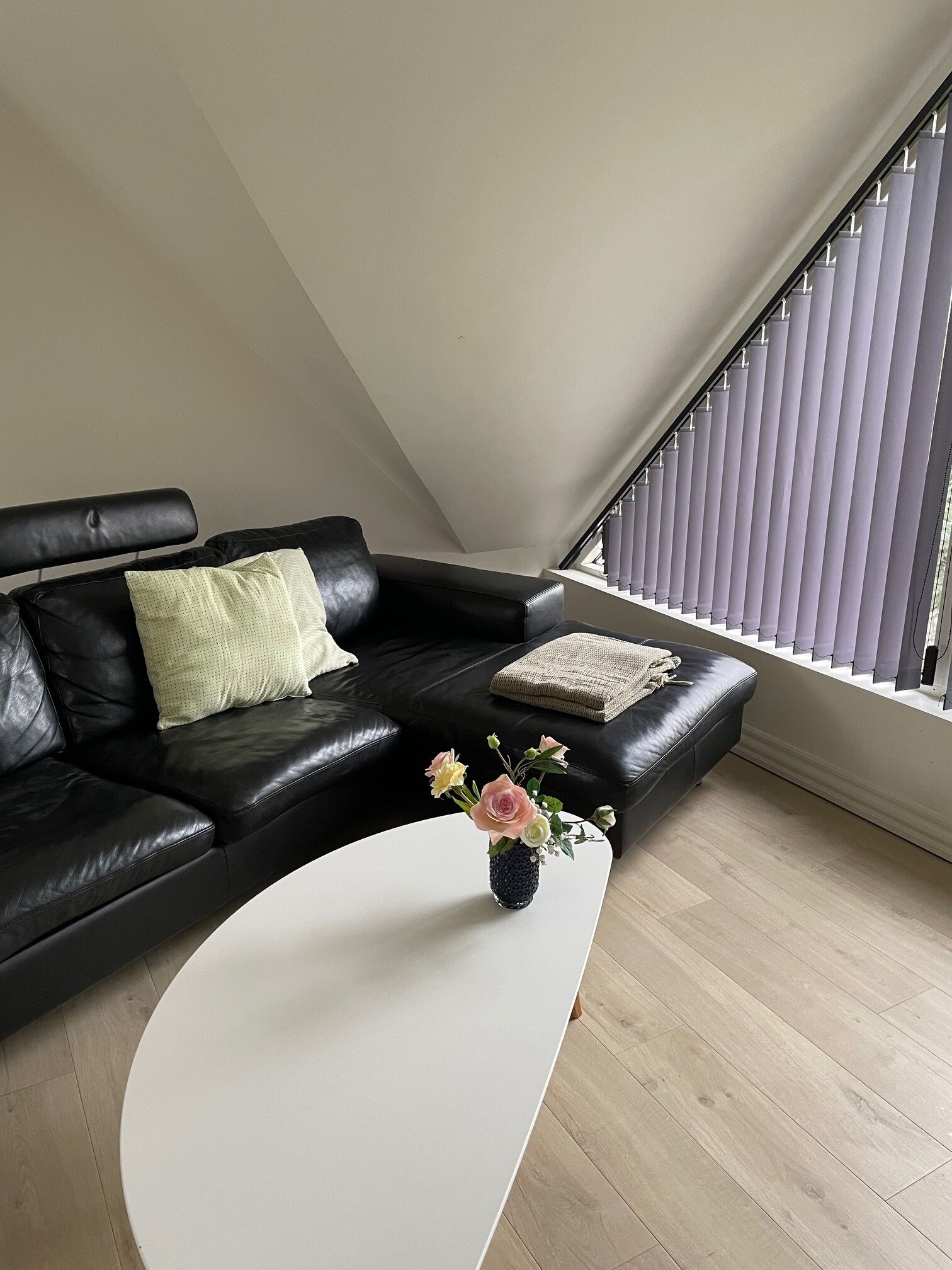 A modern living room with a black leather sofa, a white coffee table, and a small vase with flowers.