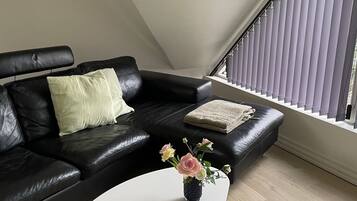 A modern living room with a black leather sofa, a white coffee table, and a small vase with flowers.