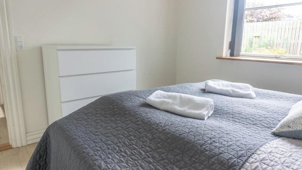 Un dormitorio con una cama, un aparador blanco y un ventanal.