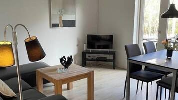 A modern living room with a sofa, a coffee table, a TV, and a dining area with chairs and a table.