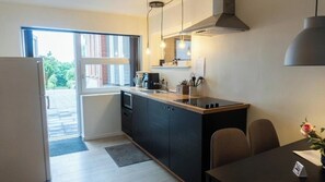A compact kitchen with a refrigerator, a sink, and a dining area with a table and chairs. - Hilmor's Lejligheder (Viborg)