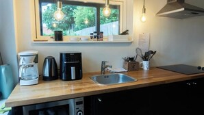 Une cuisine moderne avec un plan de travail en bois, une machine à café, un grille-pain, une bouilloire, un évier et des lampes suspendues.