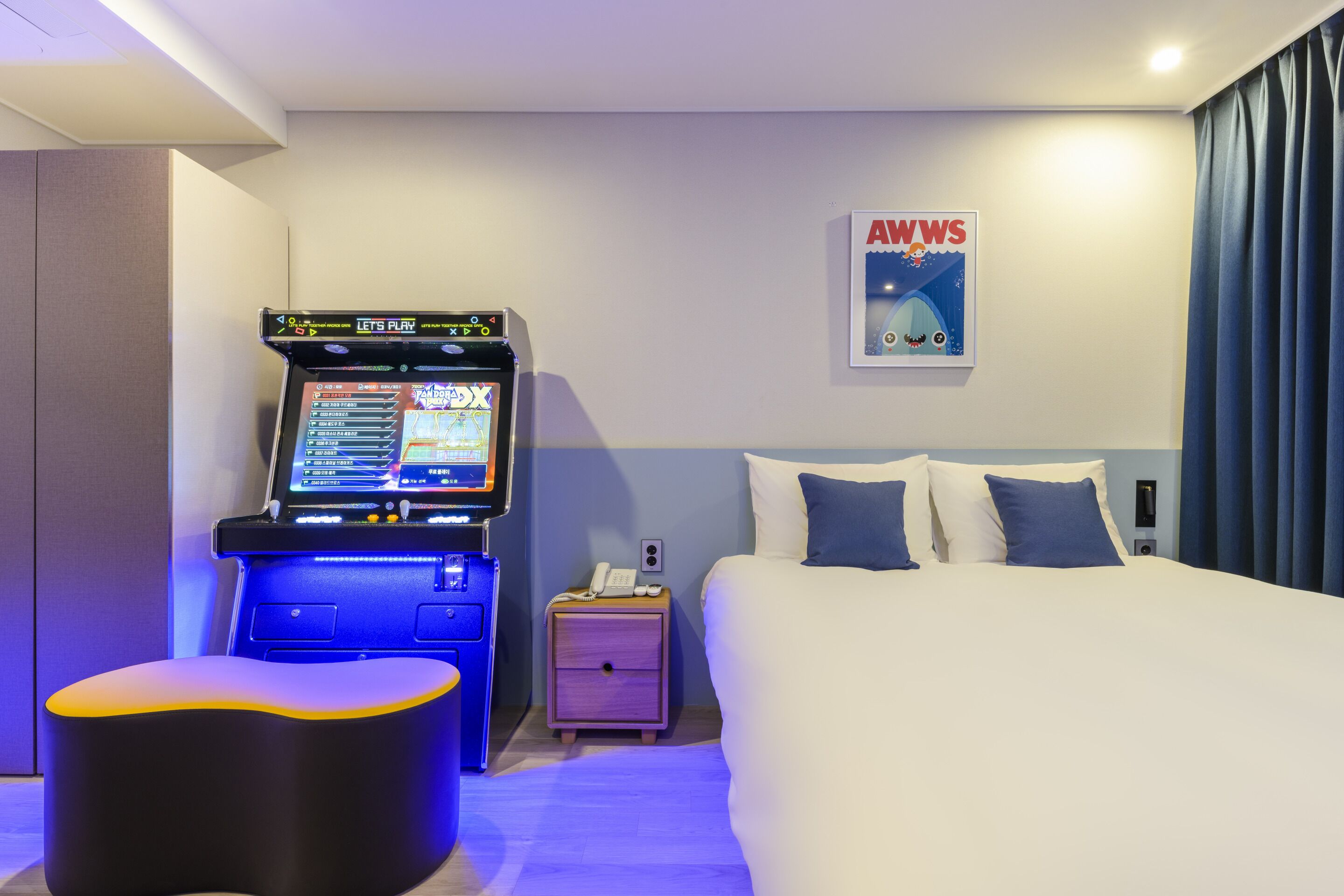 Une chambre d’hôtel avec un lit, un petit bureau avec un ordinateur, une table de chevet avec un téléphone et une affiche accrochée au mur.