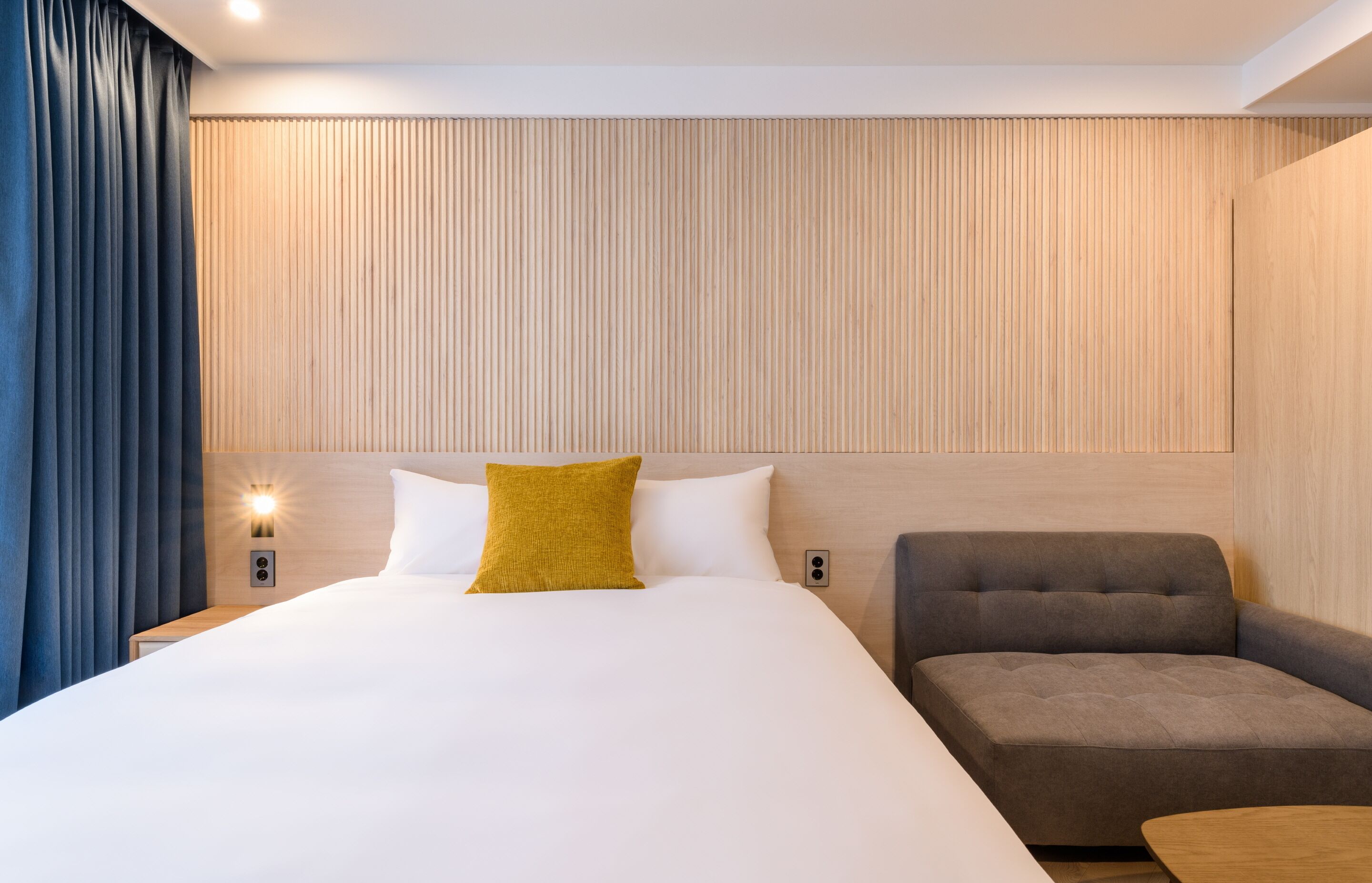 A modern hotel room with a large bed, a sofa, and a wooden accent wall.