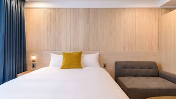A modern hotel room with a large bed, a sofa, and a wooden accent wall.