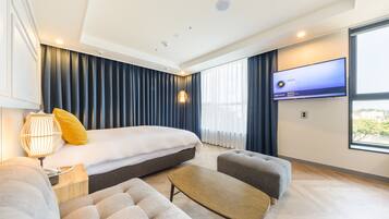 A modern hotel room with a large bed, a flat-screen TV, a sofa, and a coffee table.