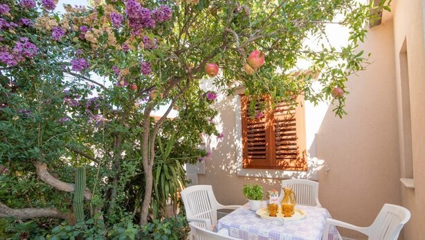 Un patio con una mesa dispuesta para dos personas, rodeado de exuberante follaje y plantas en flor.