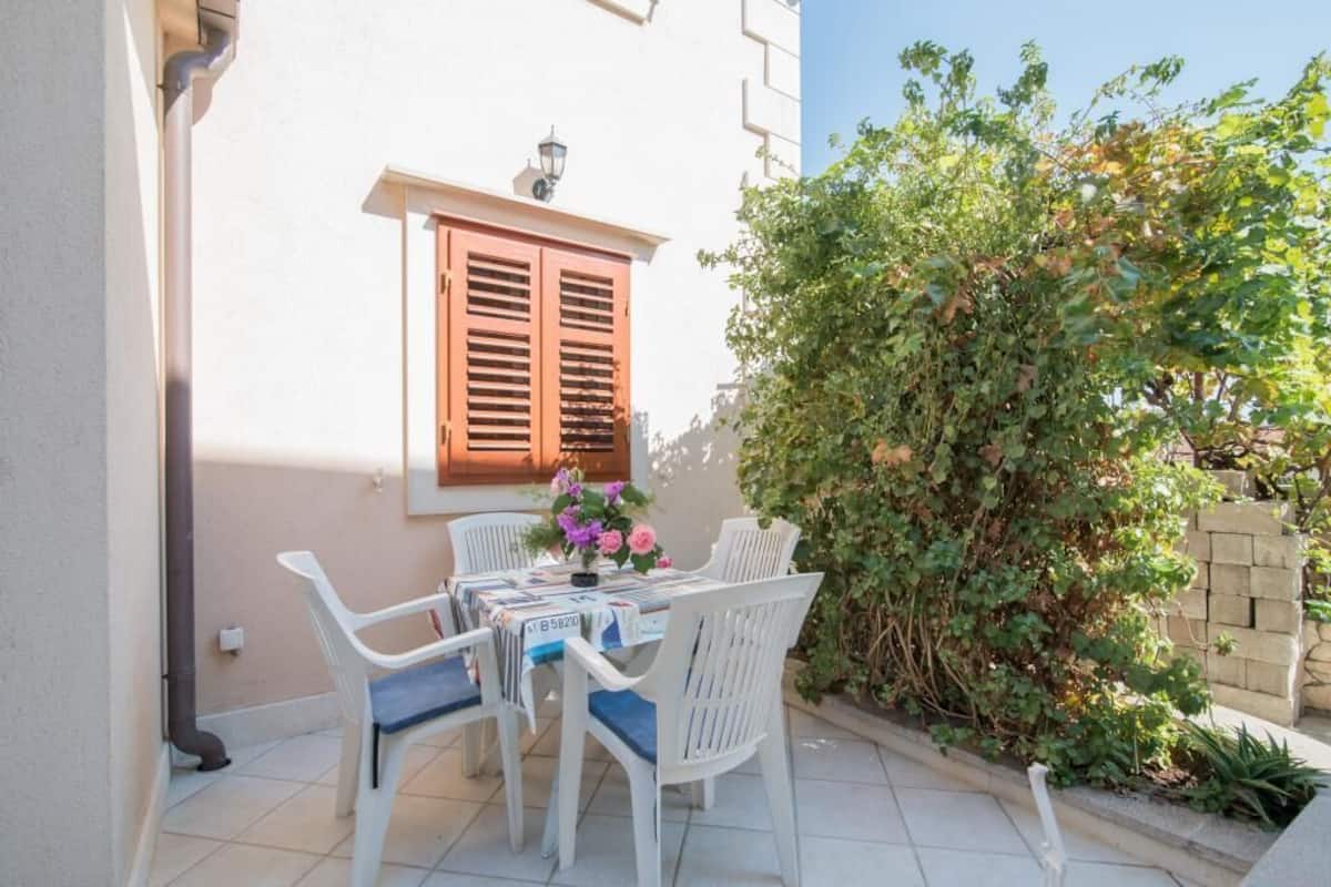 Un patio con una mesa y sillas, una ventana con persianas y un arbusto.