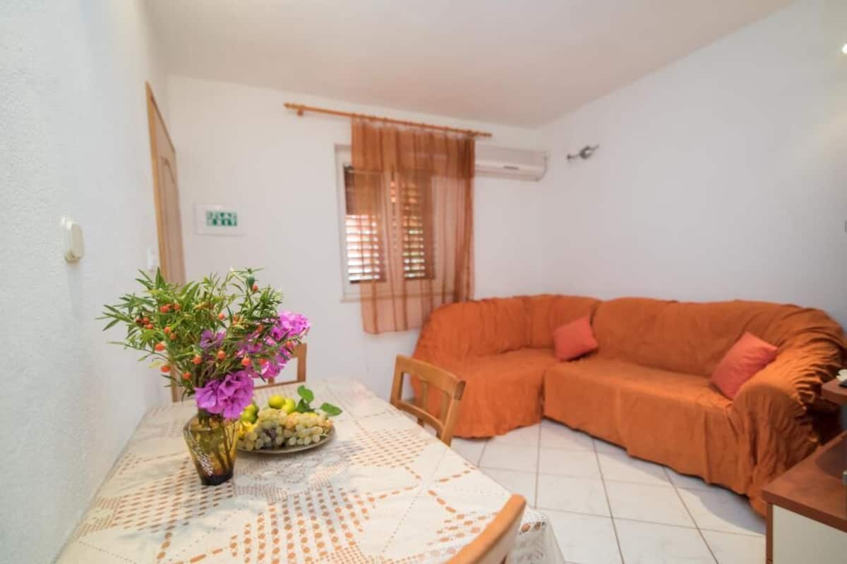 Una sala pequeña con un sofá, una mesa con un florero y una ventana con cortinas.