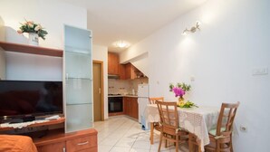Un espacio habitable compacto con televisor, muebles de madera, una mesa de comedor con sillas y una zona de cocina.
