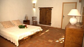 Ein Schlafzimmer mit einem hölzernen Bettgestell, einem Nachttisch, einem Sessel, einem an der Wand befestigten Schrank und einer Tür.