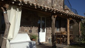 Ein Steinhaus mit einer überdachten Terrasse, einem weißen Sofa und einem Esstisch.