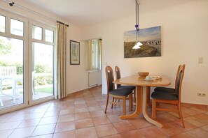 A dining area with a round table, chairs, a painting, and a view through large windows.