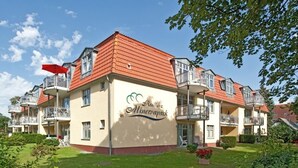 A multi-story residential building with balconies, a garden, and a clear sky.
