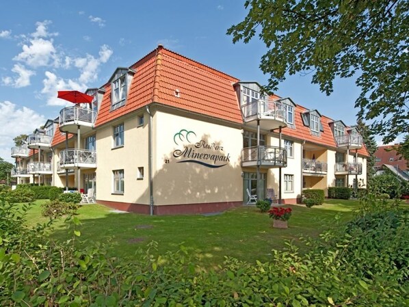 A multi-story residential building with balconies, a garden, and a clear sky.