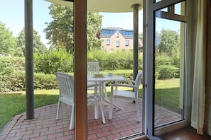 Un patio con una mesa y sillas, piso de ladrillo y vistas a un edificio y follaje.
