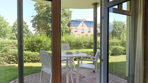 A patio with a table and chairs, a brick floor, and a view of a building and greenery.