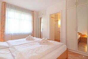 A hotel room with two beds, a wardrobe, a bathroom, and a view of the outside. - Minervapark Whg. Mi01 (Ostseebad Boltenhagen)