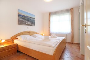 A hotel room with a bed, a nightstand, a wall-mounted picture, a window with curtains, and a door.