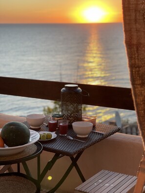 A table set with a watermelon, bowls, glasses of juice, and a candle on a balcony overlooking the ocean at sunset. - House in secure residence with exceptional sea view (tarco conca)