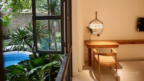 A room with a wooden table and chair, a small round mirror, and a view of a pool and greenery outside. - CityHouse VIBE City Oasis (Ho Chi Minh City)