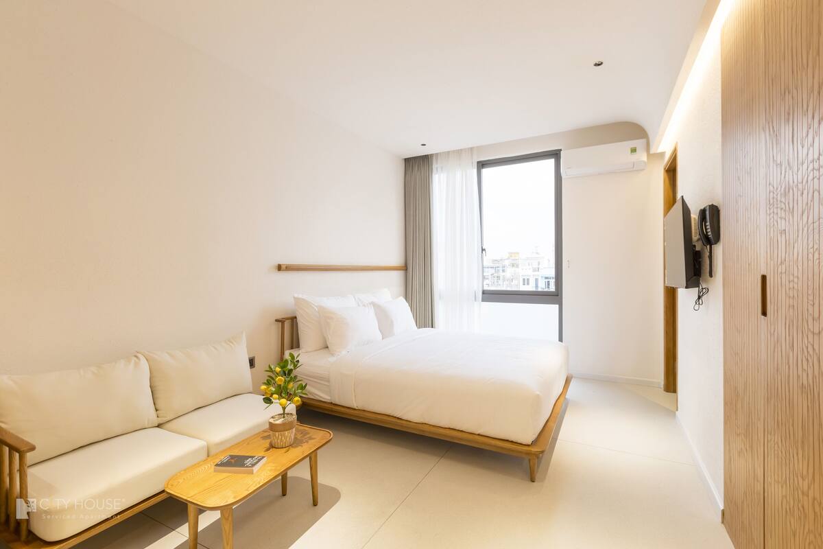 A modern hotel room with a bed, sofa, and a small table with a vase of flowers.