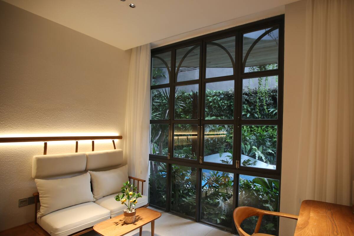 A modern living room with a sofa, a wooden coffee table, and a large window with a view of greenery.
