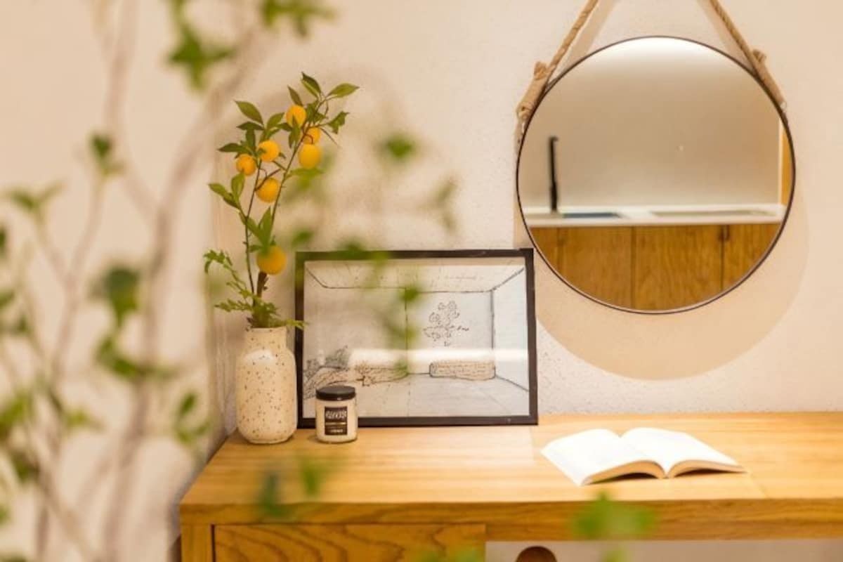 Una mesa de madera con un cuadro enmarco, un jarrón pequeño con flores amarillas, una vela y un libro abierto.