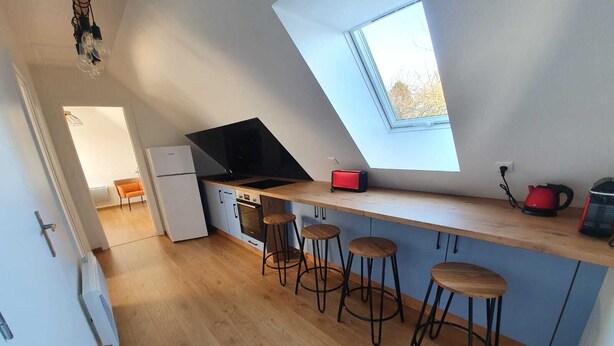 A modern kitchen with a skylight, a refrigerator, a stove, and bar stools. - Linen Granne (Petit-Caux)