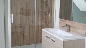 A modern bathroom with a glass-enclosed shower, a wooden vanity, and a large mirror. - Linen Granne (Petit-Caux)