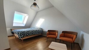 A bedroom with a bed, two chairs, a small table, and a skylight. - Linen Granne (Petit-Caux)