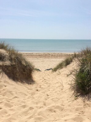 A sandy beach path leading to the ocean with dunes on either side.